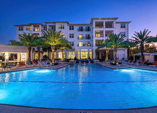 A large, well-lit swimming pool in front of a multi-story residential building.