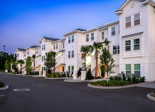 A row of white houses with trees in front.