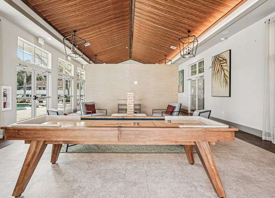 A large wooden table is in the middle of a room with a high ceiling and large windows.