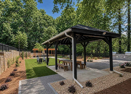 A wooden pavilion is surrounded by a gravel and grass area.