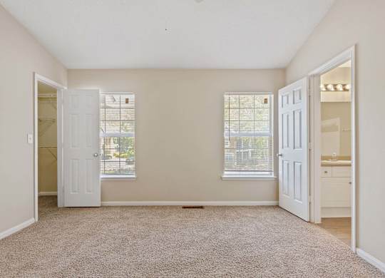 A room with a carpeted floor and two windows.