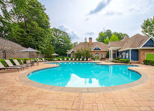 A large swimming pool surrounded by a brick patio and lounge chairs.