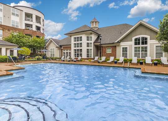 Two-Bedroom Apartments in Charlotte, NC - Gramercy Square at Ayrsley - Swimming Pool with White Loungers, Small Tables, and Umbrellas, Overlooking the Apartments.