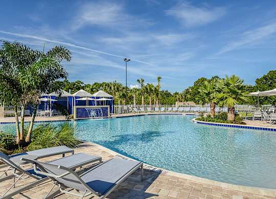 A pool surrounded by sun loungers and trees.