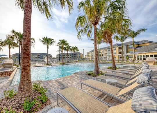 A pool surrounded by palm trees and lounge chairs.