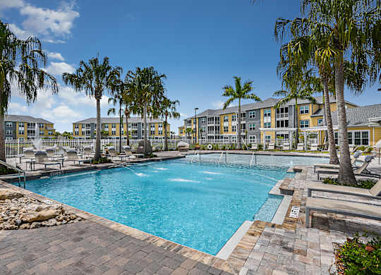A large swimming pool surrounded by palm trees and apartment buildings.