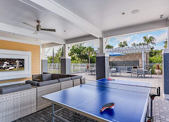 A ping pong table is in the middle of a room with a ceiling fan and a painting on the wall.