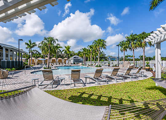 A pool area with lounge chairs and a white pergola.