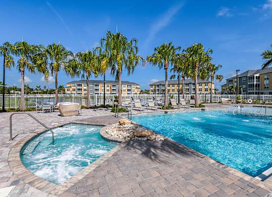 A large outdoor swimming pool surrounded by palm trees and a hot tub.
