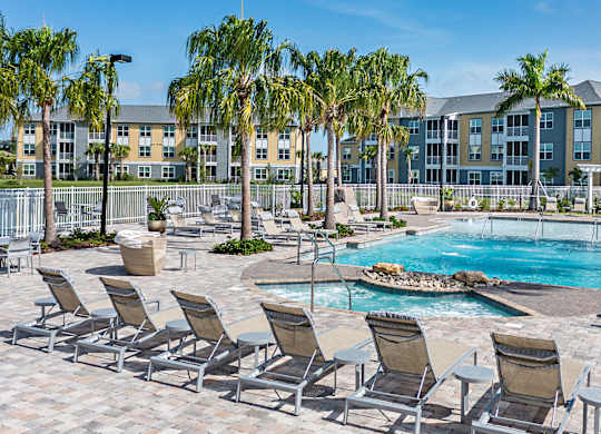 A pool surrounded by lounge chairs and palm trees.