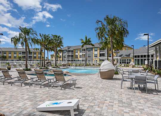 A sunny day at the poolside with chairs and palm trees.
