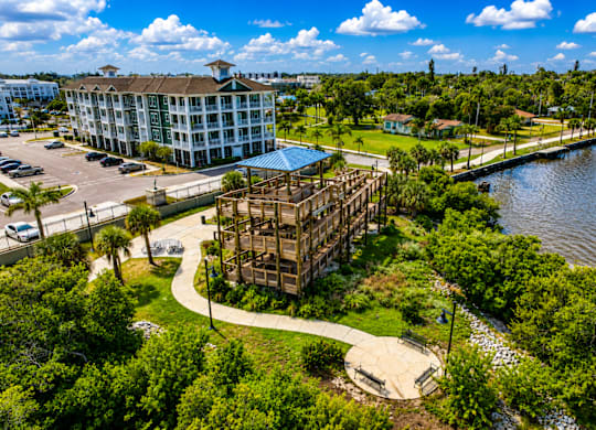 A modern building with a glass facade is surrounded by lush greenery and a body of water.