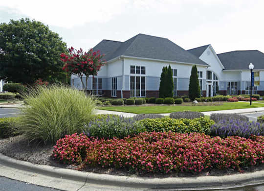 A white building with a grey roof is surrounded by a flower bed.