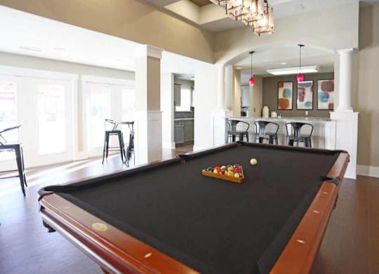 A pool table in a room with a bar and chairs.