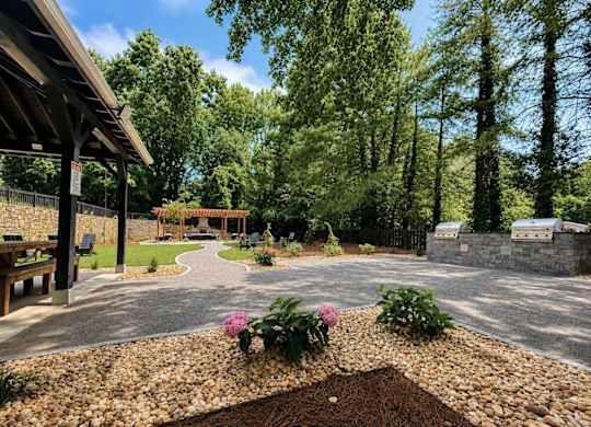 A garden with a gravel path and a bench under a wooden structure.