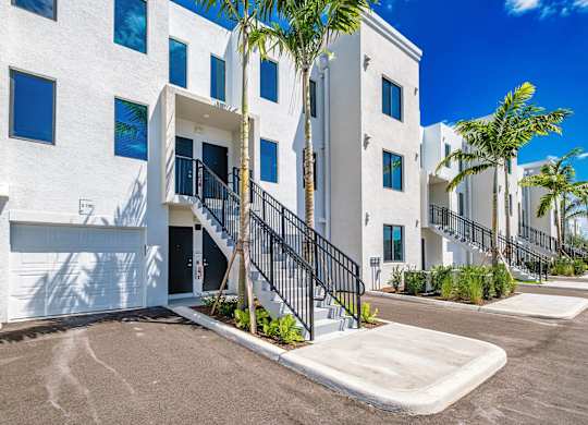 a large white building with stairs and palm trees at Altis Santa Barbara, Naples, FL