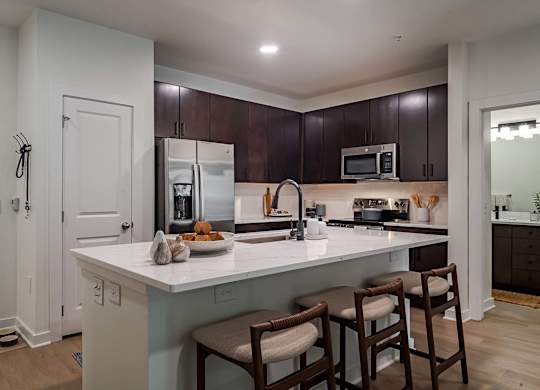 A kitchen with a white counter top and brown chairs.
