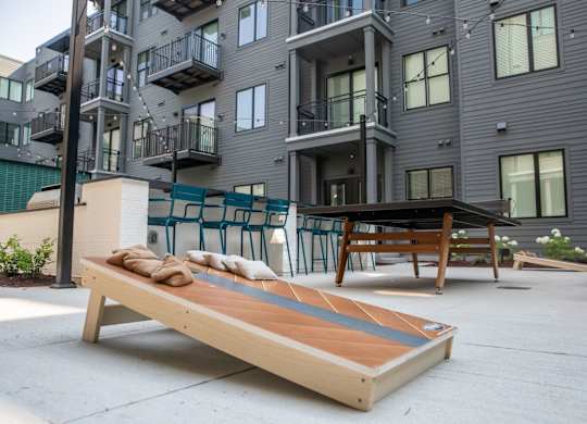 A wooden bench with cushions is in front of a modern apartment building.