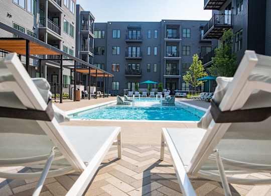 Two white chairs are facing a pool in a courtyard.