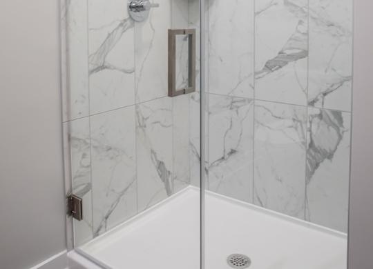 A white shower with a marble tile wall.