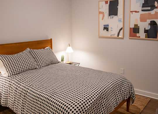 A bed with a black and white comforter sits in a room with two paintings on the wall.