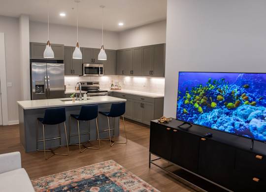 A modern kitchen with a bar area and a television displaying an underwater scene.