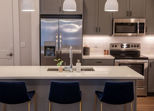 A modern kitchen with a white island and blue chairs.