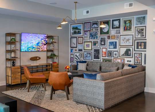 A living room with a grey couch, orange chairs, and a TV on a wooden stand.