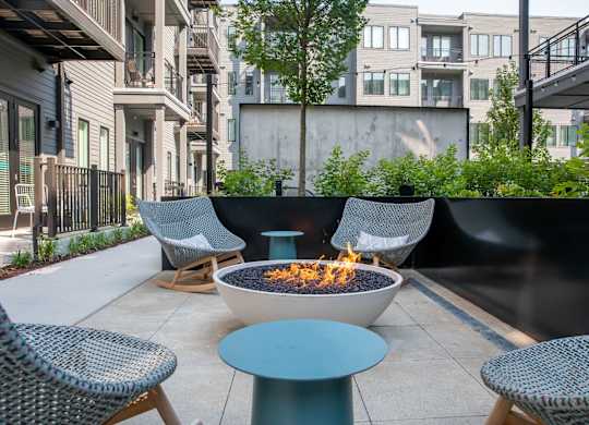 A fire pit sits in the middle of a patio surrounded by chairs.