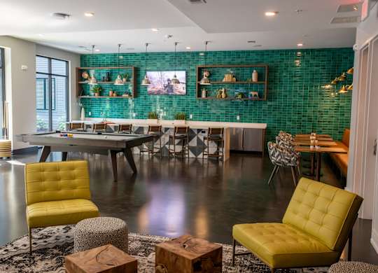 A modern living room with a green tiled wall and yellow chairs.