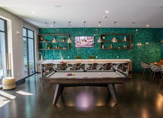 A pool table is in the middle of a room with a green tiled wall.