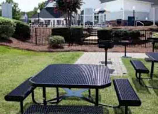 A black picnic table with two benches is in the foreground of a grassy area.