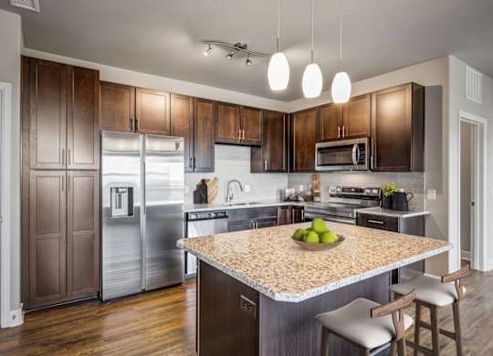 A kitchen with a granite countertop and a bowl of green apples on it.