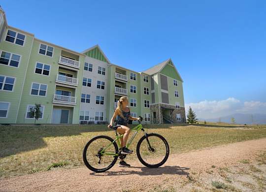 A person riding a bike in front of a green apartment building.