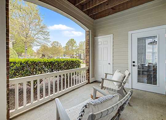 A white chair is on a porch with a view of a tree and a house.