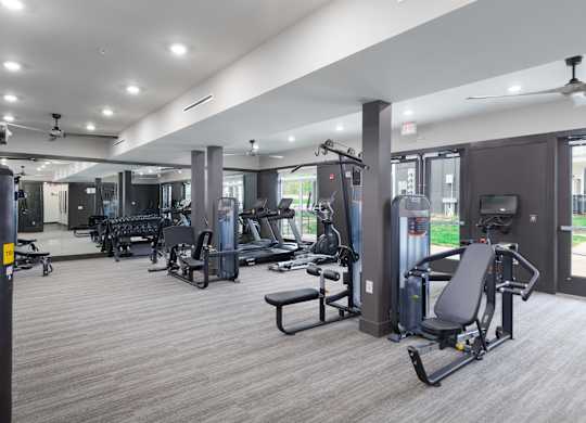 3-Bedroom Luxury Apartments in East Nashville, TN - Flats at Laurel and Pine - Fitness Center with Strength Training Equipment, Free Weights, Cardio Machines, Ceiling Fans, Mirror Wall, and Floor-to-Ceiling Windows.