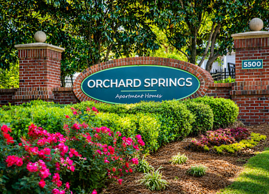 A sign that says Orchard Springs in front of a green bush.