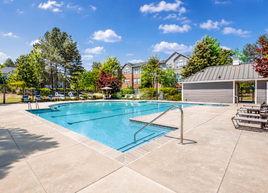 A large outdoor swimming pool surrounded by a concrete patio and a metal fence.