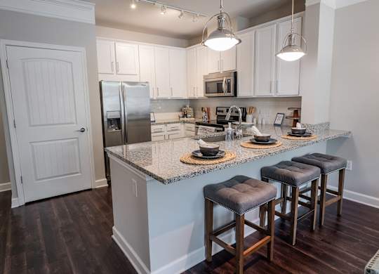 Luxury Apartments in Atlanta, GA, with an In-Unit Washer and Dryer - The Eliza on Collier - Kitchen with Breakfast Bar, Bar Stools, Granite Countertops, White Cabinetry, and Stainless Steel Appliances.