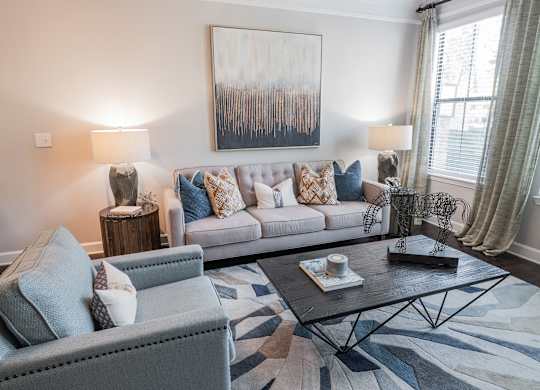 Atlanta, GA, Luxury Apartments with In-Unit Washer and Dryer - The Eliza on Collier - Living Room with Couch, Armchair, Coffee Table, Side Tables, Lamps, Wall Art, and Large Window.