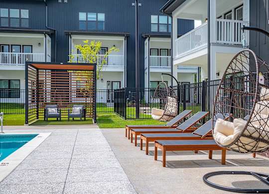 a patio with lounge chairs and a swing in front of an apartment building