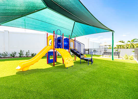 A playground with a yellow slide and a blue slide under a green canopy.