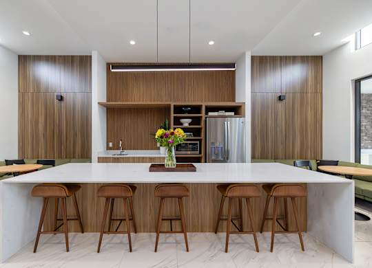 A modern kitchen with a long white island and wooden stools.