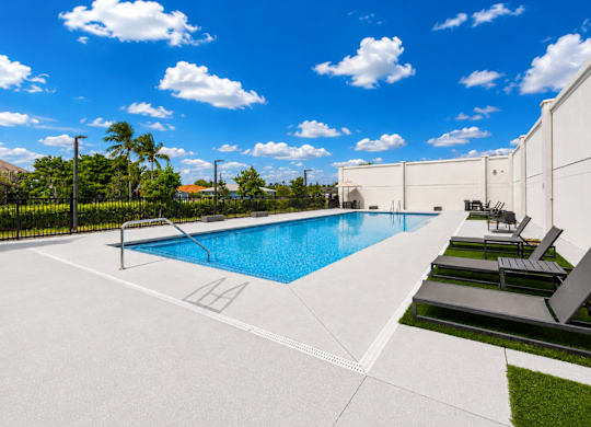 A swimming pool with lounge chairs and a white fence.