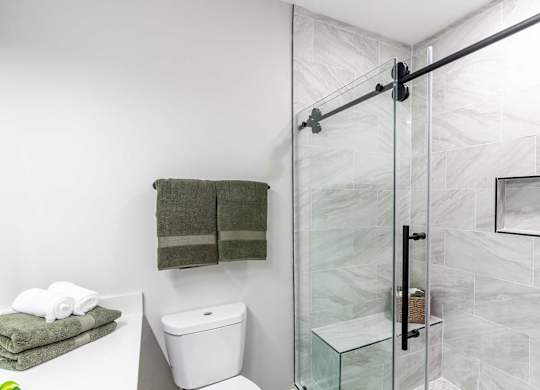 A bathroom with a toilet, a towel, and a glass shower door.