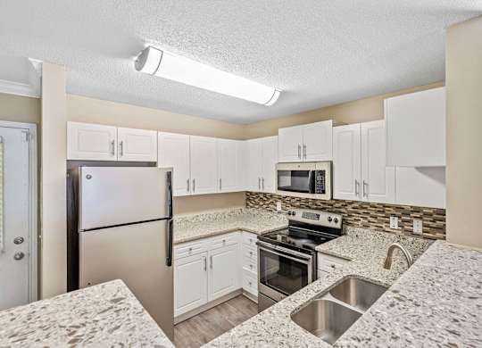 Townhomes for Rent in Loganville, GA - Alexander Crossing - Modern Kitchen With White Cabinets, Granite Counters, Stainless Steel Appliances, and Double Sink With Mosaic Backsplash.