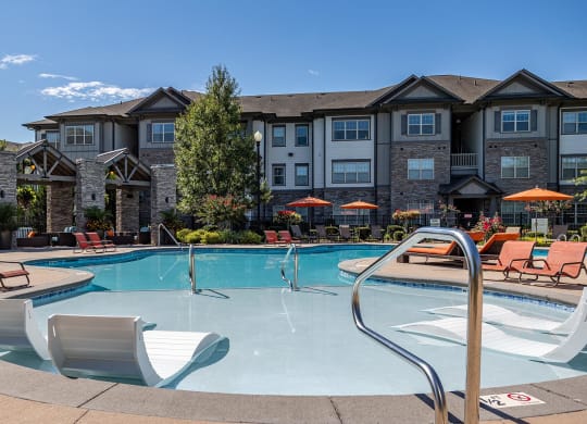 a swimming pool with chairs and a building in the background