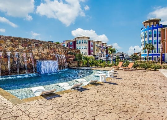 a swimming pool with a waterfall and buildings in the background