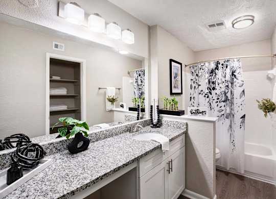 A bathroom with a granite countertop and a shower with a floral shower curtain.