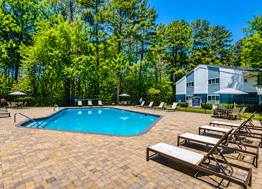 A pool surrounded by trees and chairs.